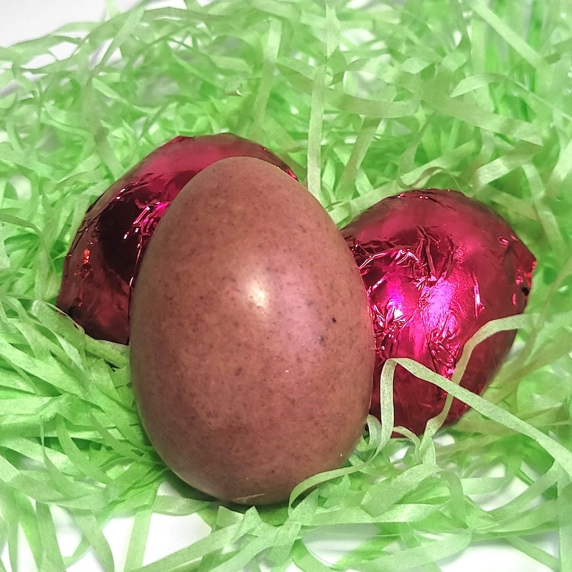 Vegan white chocolate Easter eggs with BC strawberry, lemon, and dragon fruit, wrapped in pink foil and shown unwrapped in spring grass - Viva Cacao!